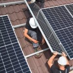 Men technicians mounting photovoltaic solar moduls on roof of house.